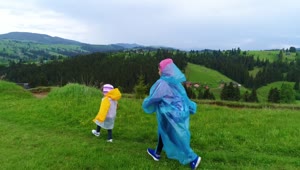 Stock Video Happy Sisters Walking Through The Field Wearing Raincoats Animated Wallpaper