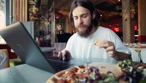 Stock Video Man Eats Pizza While Woking On Laptop At Hip Cafe Animated Wallpaper