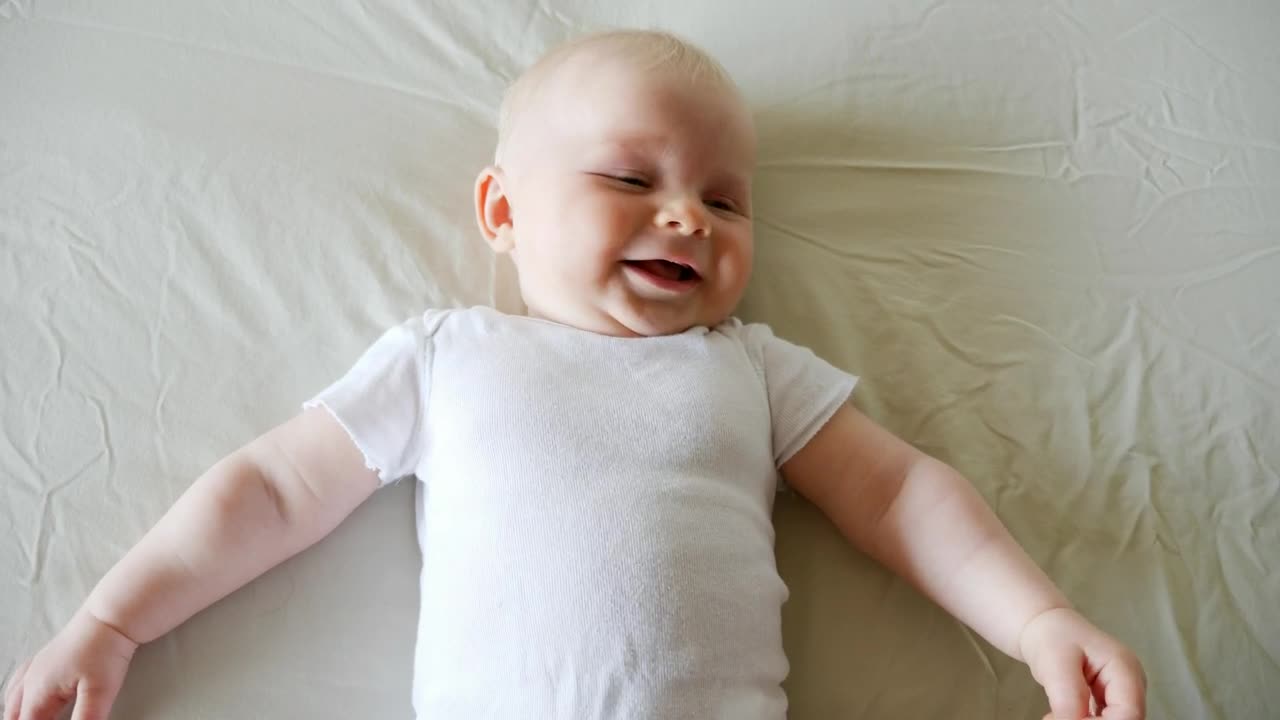 Download Stock Video Laughing Baby Lying On Bed In White Onesie Animated Wallpaper