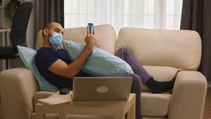 Stock Video Man With Coronavirus On Sofa With Mobile Phon Animated Wallpaper