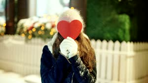 Free Video Stock Smiling Woman Covers Face With Heart Cutout In Snowy Street Live Wallpaper